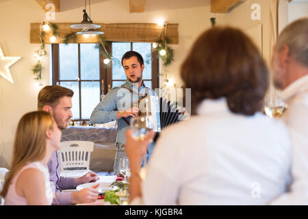 Young man playing accordion for family at Christmas dinner table Stock Photo