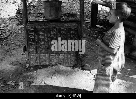 Black and white photograph of a depression era sharecropper's child, a boy, standing in front of a small stove made with license plates, Arkansas, 1935. From the New York Public Library. Stock Photo