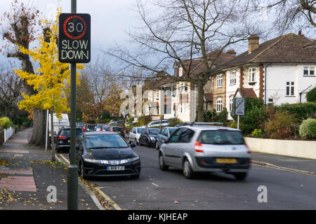 A car (motion blurred) speeds past an illuminated vehicle activated speed sign on a suburban residential road Stock Photo