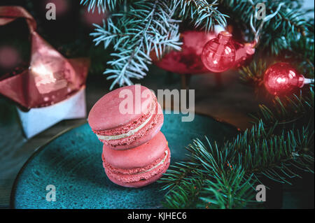 Fresh red macaroons at the Christmas table with the garland on the Christmas tree branches. Copy the place. The horizontal frame. Stock Photo