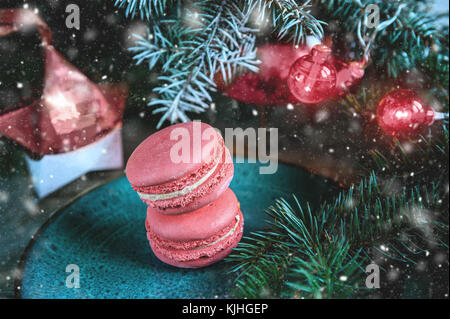 Fresh red macaroons at the Christmas table with the garland on the Christmas tree branches. Copy the place. Snow. The horizontal frame. Stock Photo