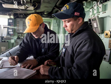 ATLANTIC OCEAN (Nov. 11, 2017) Lt. j.g. Grant Ellis, from Fort Worth, Texas, reviews a deck log prepared by Quartermaster 2nd Class Anthony Summerour, from Atlanta, on the bridge of the amphibious assault ship USS Iwo Jima (LHD 7). Iwo Jima, components of the Iwo Jima Amphibious Ready Group and the 26th Marine Expeditionary Unit are conducting a Combined Composite Training Unit Exercise that is the culmination of training for the Navy-Marine Corps team and will certify them for deployment. (U.S. Navy photo by Mass Communication Specialist Seaman Michael H. Lehman/Released) Stock Photo