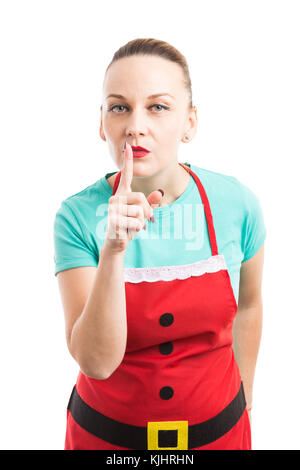 Woman wearing red Christmas apron making shush silence gesture by touching index finger on lips isolated on white background Stock Photo