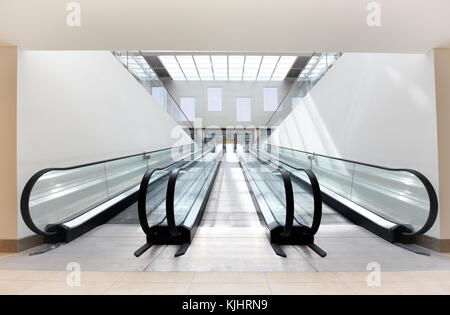 Two empty escalators, one ascending and one descending, side by side in a brightly lit commercial building Stock Photo