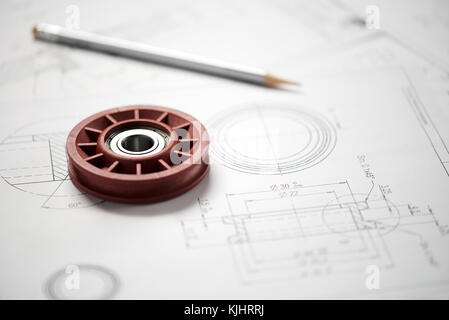 Plastic wheel bearing and grey pencil over blueprint with project drawings, close-up shot from high angle Stock Photo