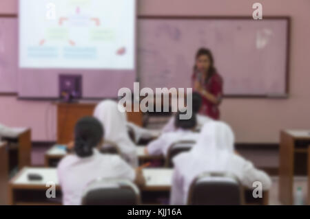 Blurred abstract background of university students sitting in a lecture room with teacher in front of the class with white projector slide screen: Blu Stock Photo