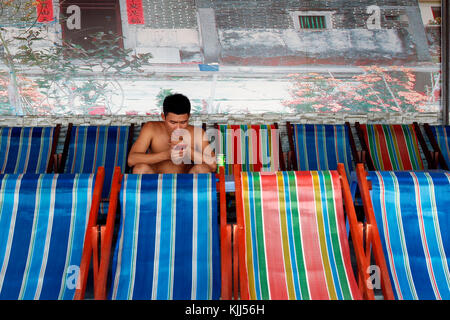 Young man using his smartphone in a Vietnamese coffee.  Vung Tau. Vietnam. Stock Photo