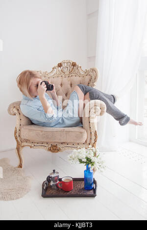 Young woman taking pictures while sitting on armchair at home Stock Photo