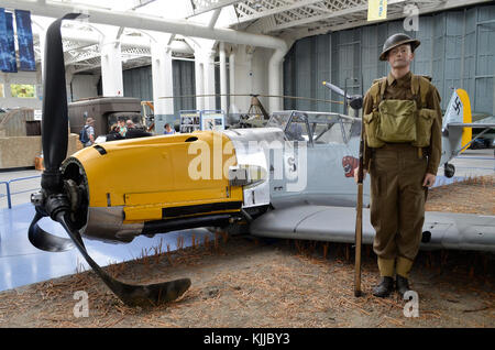 Messerschmitt Bf109E, Duxford IWM, UK, with British sentry recreating a Battle of Britain scene. This Bf109E was shot down and belly landed in 1940. Stock Photo