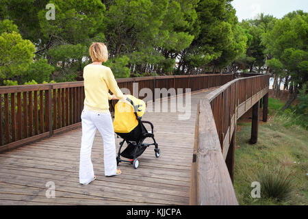 Blond hair woman strolling a baby in carriage Stock Photo