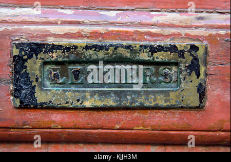 Letterbox on a very old, weathered red door. Stock Photo