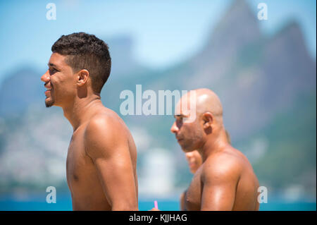 RIO DE JANEIRO - FEBRUARY 9, 2017: Brazilian surfers stand on the beach at Arpoador, the popular surf spot, against a skyline view of two brothers mou Stock Photo