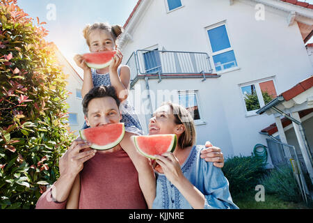 Portrait of happy family with slices of watermelon in front of their home Stock Photo