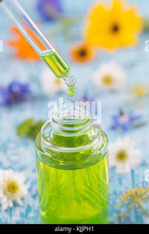 tranparent glass bottles with drops Essential liquid in dropper on wooden background with medicinal flowers Stock Photo