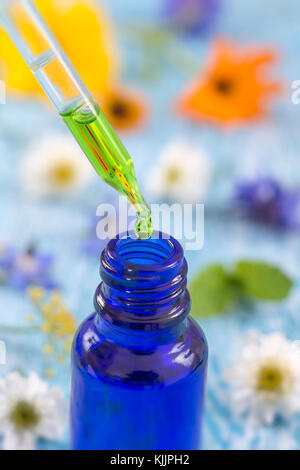 tranparent glass bottles with drops Essential liquid in dropper on wooden background with medicinal flowers Stock Photo