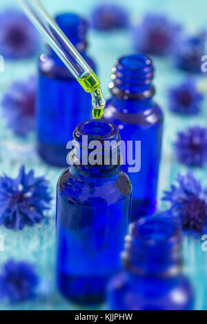 tranparent glass bottles with drops Essential liquid in dropper on wooden background with medicinal flowers Stock Photo