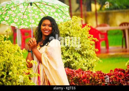 Indian girl In sari walking in the rain with umbrella, Pune, Maharashtra. Stock Photo