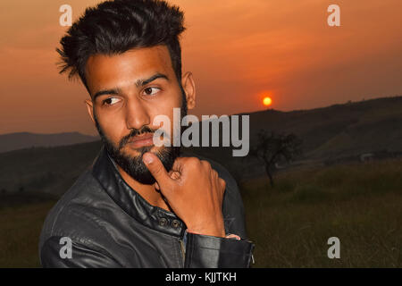 Indian Boy Posing On Motor Bike Near Mountain At Sunset, Pune, Maharashtra. Stock Photo