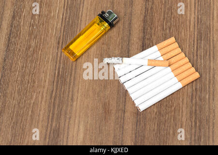 Tobacco and lighter,  burning cigaretter detrimental on wood background ,select focus front  cigaretter Stock Photo