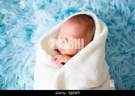 Little cute newborn baby boy, sleeping wrapped in white wrap, holding little knitted toy Stock Photo