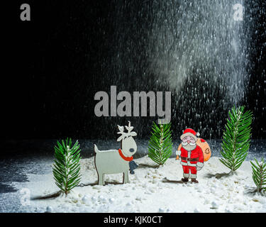 New Year's background. Figures of Santa Claus, deer and boy. Snow angel. Snowing. Night frame. Billet for postcards or congratulations. Copy space Stock Photo