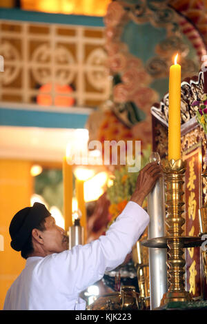 Cao Dai Holy See Temple.  Priest lighting candle on altar for  12 o'clock ritual.  Thay Ninh. Vietnam. Stock Photo