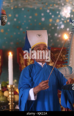 Cao Dai Holy See Temple.  High priest lighting candle on altar for  12 o'clock ritual.  Thay Ninh. Vietnam. Stock Photo