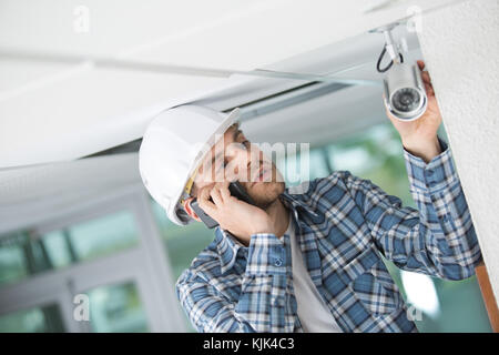 Contractor checking security camera and talking on telephone Stock Photo