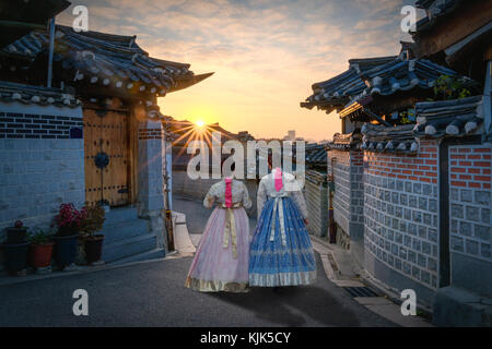 Back of two women wearing hanbok walking through the traditional style houses of Bukchon Hanok Village in Seoul, South Korea.