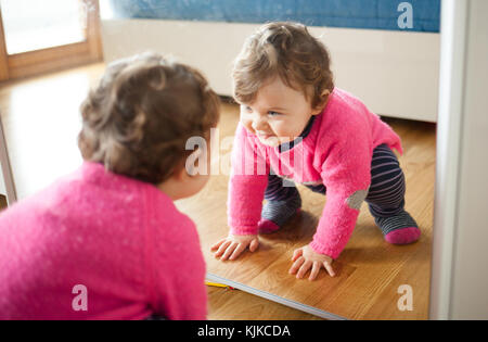 Toddler baby girl playing with mirror in the bedroom. Stock Photo