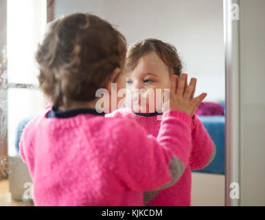 Toddler baby girl playing with mirror in the bedroom. Stock Photo