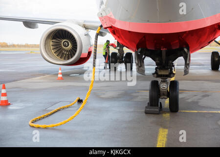 Commercial airplane being charged while worker working on wet runway Stock Photo