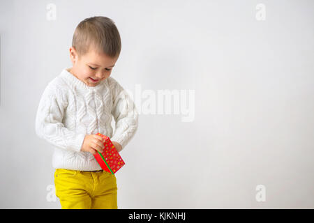 A happy smiling  boy in a white sweater and yellow jeans is takes out a gift. Child looking of a red cardboard box. Isolate on white background. Chris Stock Photo