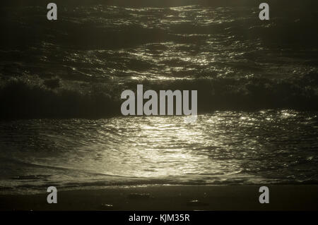 Golden light on the stormy sea and waves on the sandy shore Stock Photo