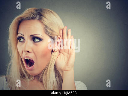 Shocked woman holds her hand near ear and listens carefully isolated on gray background Stock Photo