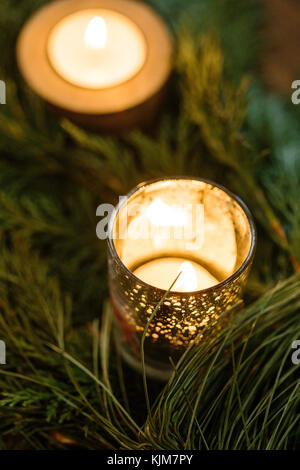nature, winter, decor concept. close up of small burning candles in different holders with silver dots, that shine like stars, both of them are hiden among the fuzzy spruce needles Stock Photo