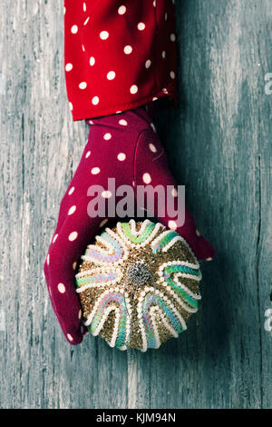 closeup of a caucasian woman wearing a red glove patterned with white dots holding an ornamented christmas ball in her hands against a gray rustic woo Stock Photo