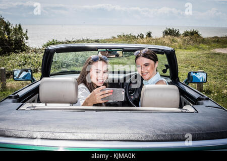Two beautiful young women on a summer road trip together in a convertible car. Stock Photo