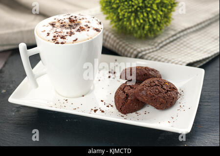 ustic cookies with cocoa and pistachios on white tray, ceramic foam cup with cappuccino and cocoa powder, cloth tablecloth and other kitchen items in  Stock Photo