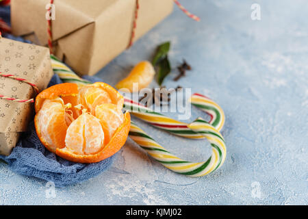 Fresh mandarins with leaves, candy canes, gift boxes in kraft paper and spices - cinnamon, anise and cloves on a blue background Stock Photo