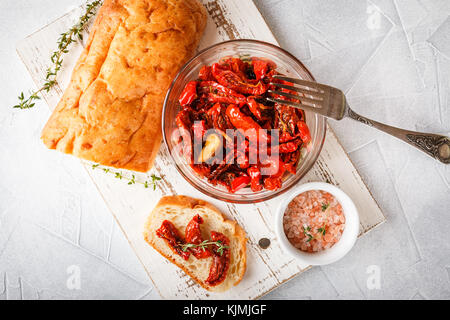 Sun dried tomatoes in glass jar on white cutting board on light background. Top view. Stock Photo