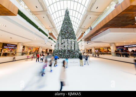 Children and Young Adults Ice Skating Around Christmas Tree in Skate Rink in a Large Indoor Shopping Mall Stock Photo