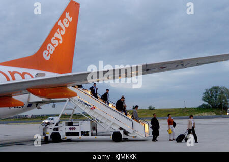 passengers disembarking a remote parked easyJet 737 via the rear Swissport airstairs at night and a woman with carry-on baggage Stock Photo