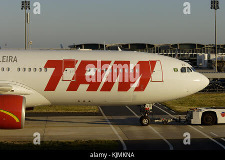 towed by a tug along a taxiway and crossing an airside vehicle road with a big TAM logo on the fuselage Stock Photo