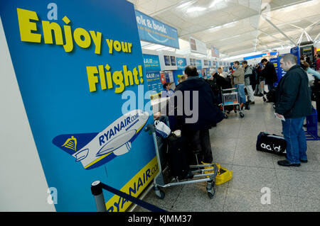 Ryanair passengers in a queue for check-in in the main terminal with an 'Enjoy your Flight' poster Stock Photo