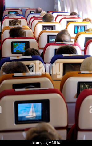 passengers sitting in the economy-class cabin with seat-back video screens LGW-ANU Stock Photo