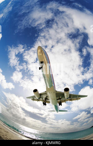 very low on final-approach to landing over Maho Beach with clouds behind Stock Photo