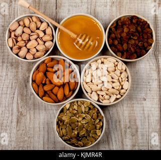 Pistachios, almonds, peanuts, pumpkin seeds, raisins and honey in ceramic plates. On the wooden table. Healthy eating Stock Photo