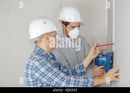 young builder in hardhat sanding wall indoors Stock Photo