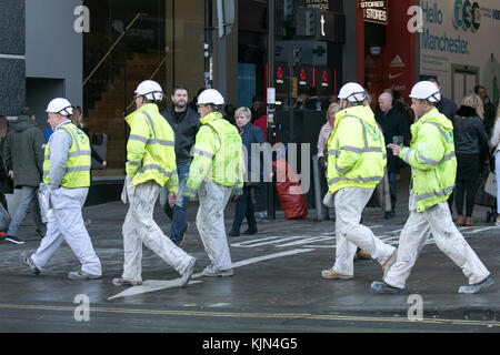 A group of professional painting contractors, workmen in hi-vis & hard hats walking across the road in Manchester city centre, UK Stock Photo